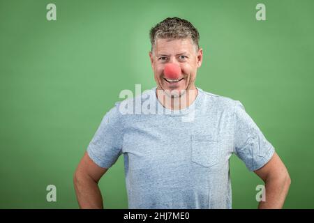 homme au nez clown rouge et chemise grise sur fond vert Banque D'Images