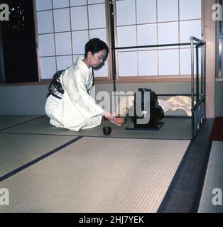 1960s, historique, une dame japonaise dans un kimono, l'hôte, s'agenouillant par le récipient de thé sur un tatami mat, dans le coin d'une salle traditionnelle de thé ou de tatami, Japon.Avec leur propre style et design unique, ces salons de thé remontent à la période de Muromachi où la boisson de thé est devenue populaire et a subterlement développé en une forme de rassemblement spirituel avec l'accent sur la simplicité et la tranquillité.Imprégnée de l'histoire et de la culture japonaises, la cérémonie du thé est un moyen de préparer et de boire du thé vert dans une atmosphère zen calme, distincte du rythme hétique normal de la vie quotidienne. Banque D'Images