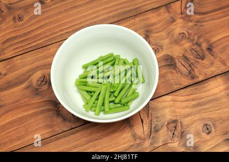 Bol blanc rempli de haricots verts hachés placé sur un fond de bois de couleur chêne Banque D'Images