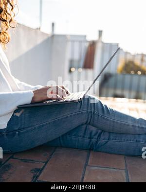 Gros plan d'une femme méconnaissable travaillant avec son ordinateur portable assis sur le sol de la terrasse Banque D'Images