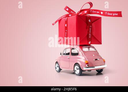 Voiture-jouet rétro rose livrant boîte-cadeau rouge avec ruban sur fond rose. Copier l'espace. Banque D'Images