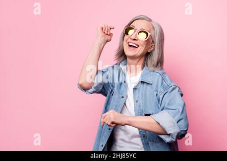 Photo de folle femme senior danse look vide espace port lunettes bleu chemise isolée sur fond rose pastel Banque D'Images