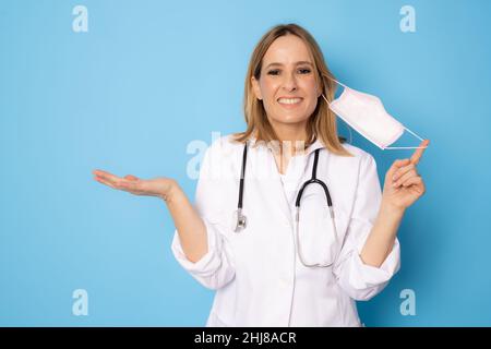 Jeune femme médecin confiante portant un masque chirurgical isolé sur fond bleu. Banque D'Images