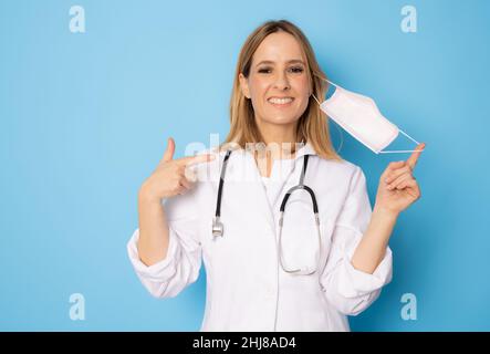 Jeune femme médecin confiante portant un masque chirurgical isolé sur fond bleu. Banque D'Images