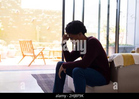 Jeune homme afro-américain avec la tête dans la main assis à la maison. Unaltered, style de vie, contemplation, dépression, tristesse et concept de vie domestique. Banque D'Images