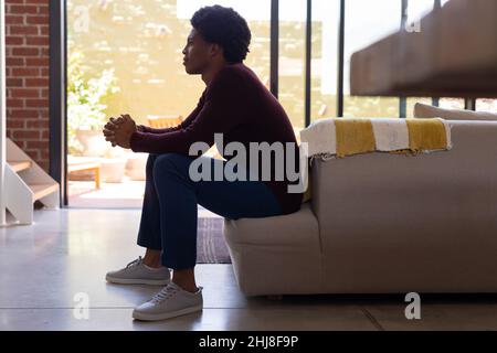 Il y a plein de jeunes afro-américains réfléchis aux mains clamées assis sur le canapé à la maison. Sans modification, style de vie, contemplation, rêve de jour, de Banque D'Images