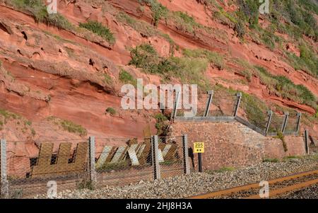 Falaises de grès rouge et filets de chute de roche le long de la ligne de chemin de fer côtière à Dawlish, dans le sud du Devon. Banque D'Images