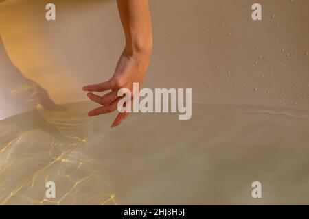 Petite main de jeune femme biraciale touchant l'eau ondulée dans la baignoire au spa. Spa, soins du corps, style de vie et bien-être. Banque D'Images