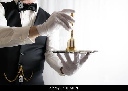 Portrait de maître d'hôtel ou de garçon en gants blancs tenant une cloche d'or sur un plateau de service argenté Banque D'Images