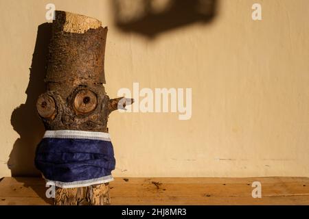 gnome de bois ou log avec masque anti-covid, penchée à l'extérieur d'une maison rurale dans les bois. Banque D'Images