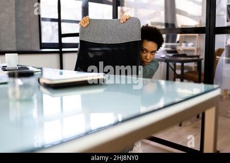 Femme effrayée se faisant cacher sous le bureau dans le bureau Banque D'Images