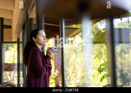 Vue latérale de la jeune femme biraciale avec le vitiligo regardant loin tout en prenant un café à la maison Banque D'Images