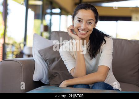 Portrait d'une jeune femme biraciale heureuse avec main sur le menton assis sur le canapé à la maison Banque D'Images