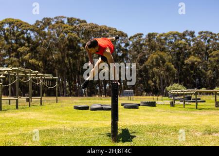 Homme de forme caucasienne sautant sur un obstacle en bois pendant un parcours d'obstacle au camp de chaussures Banque D'Images