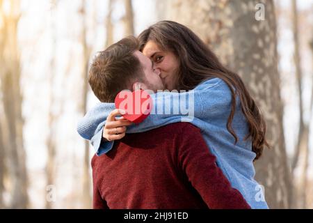 L'homme surprend sa petite amie avec un cadeau en forme de coeur et elle l'embrasse Banque D'Images