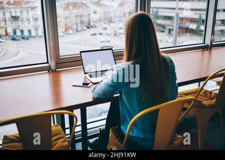 Femme utilisant un ordinateur portable à la table près de la fenêtre Banque D'Images