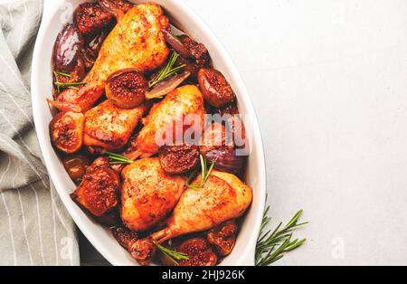 Cuisses de poulet cuites au four, pilons de figues et oignons rouges dans un plat de cuisson en céramique, fond de table de cuisine blanche, vue du dessus Banque D'Images