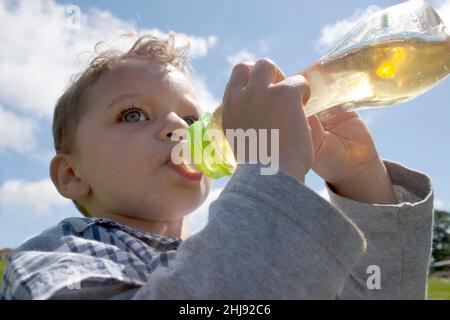 tout-petit buvant du jus de pomme provenant d'un biberon Banque D'Images