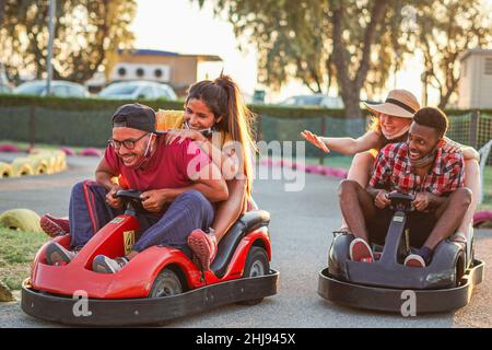 Groupe d'amis multiraciaux s'amusant avec Go kart - jeunes avec masque de visage sur sourire et gai à la course de mini-voiture - couples à l'extérieur à faire Banque D'Images