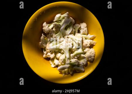 Morceaux de chou-fleur hachés dans un bol jaune à fond noir.Mise au point sélective Banque D'Images