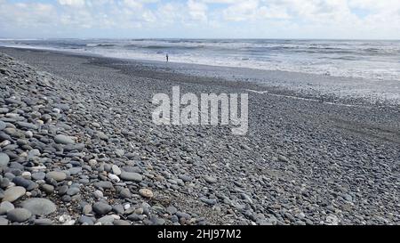 Une personne éloignée au bord des vagues sur une grande plage de sable sur la côte ouest de la Nouvelle-Zélande Banque D'Images