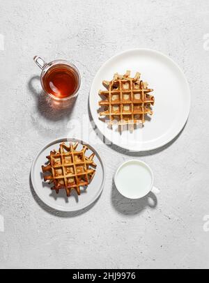 Gaufres belges fraîchement cuites sur des assiettes blanches, lait et thé sur une table légère, concept de petit déjeuner savoureux, vue sur le dessus Banque D'Images