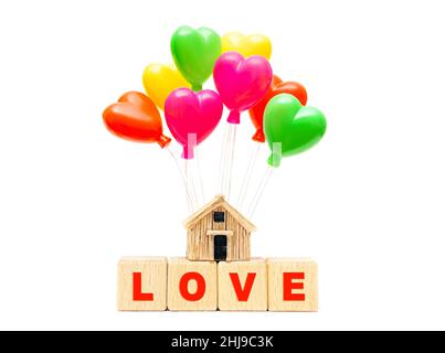 Mot AMOUR fait de blocs de lettres en bois et un modèle de maison miniature avec des ballons de jouet en forme de coeur isolés sur fond blanc.Concept Homeplénitude Banque D'Images