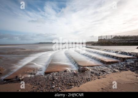 Longue exposition de la cascade de la rivière Avill qui coule sur la plage de Dunster dans le Somerset Banque D'Images