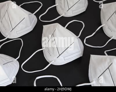 De nombreux masques anti-poussière blancs KN95 propres et inutilisés sont affichés sur un fond noir Uni. Banque D'Images
