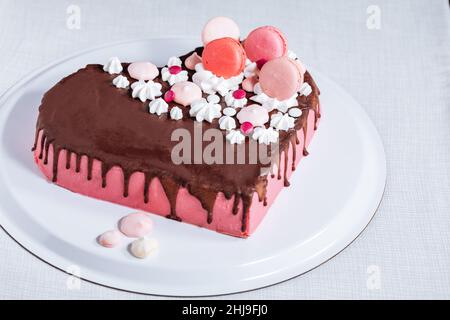 Vue de dessus de gâteau en forme de coeur rose avec glaçure de chocolat, meringues et macarons sur le dessus comme décoration.Saint-Valentin, Fête des mères. Banque D'Images