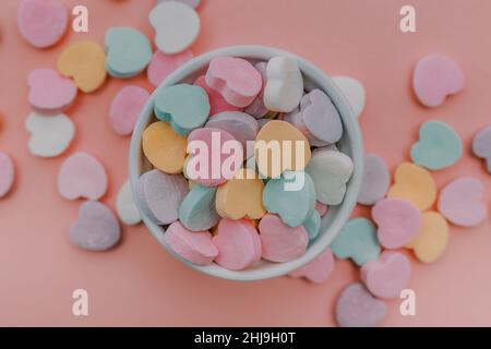 Saint-Valentin conversation couleur pastel coeur bonbons qui se répande du bol blanc sur fond rose clair Banque D'Images