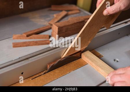 Menuisier sciant le détail du bois sur une scie circulaire à boulonner avec un bâton pour travailler en toute sécurité Banque D'Images