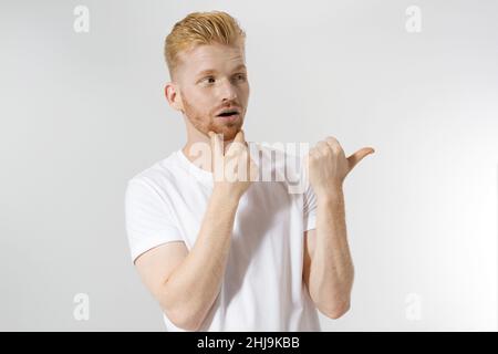 Joyeux jeune homme à tête rouge, barbe élégante rouge isolée.Homme pointant l'espace de copie pour la publicité.Homme en t-shirt blanc, coupe de cheveux tendance.Jeune e réussi Banque D'Images