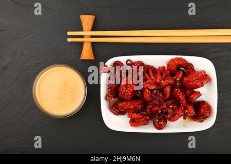 Gros plan de la petite salade de poulpes rouges entières de fruits de mer avec sauce satay et baguettes sur fond de tableau d'ardoise noire, vue du dessus en hauteur, dir Banque D'Images