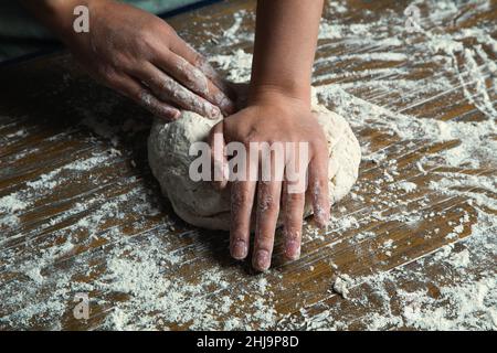 Une photo d'une femme chef boulangère dans une cuisine pétriant de la farine dans une pâte à pain artisanale fraîchement préparée. Banque D'Images