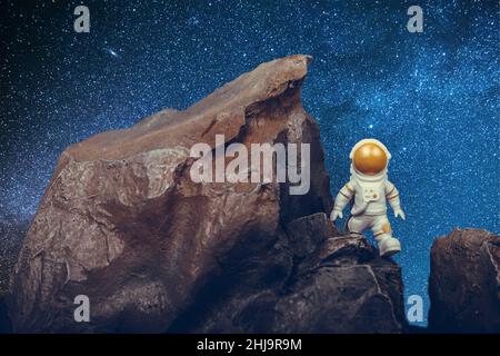 Astronaute déterminé avec visière dorée et combinaison blanche sur la surface rocheuse avec fond spatial. Banque D'Images