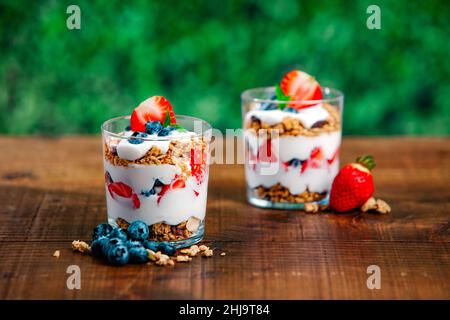 Parfait de yaourt à la vanille avec fraise, myrtille et granola placé sur une table de pique-nique extérieure en été. Banque D'Images