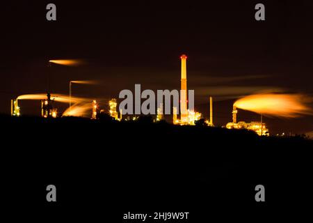 Une raffinerie de pétrole avec une pollution de fumée jaune qui s'élève dans le ciel noir foncé de nuit. Banque D'Images