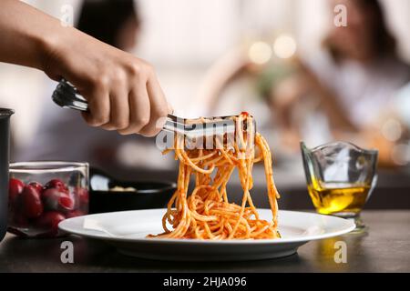 Femme mettant de savoureuses pâtes Puttanesca sur l'assiette à table dans le restaurant Banque D'Images