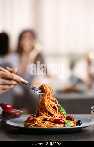 Femme mettant de savoureuses pâtes Puttanesca sur l'assiette à table dans le restaurant Banque D'Images