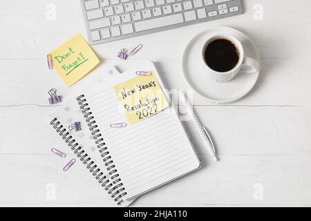 Tasse de café, clavier d'ordinateur, papeterie, notes adhésives avec texte NOUVELLE ANNÉE RÉSOLUTION 2022 et N'OUBLIEZ PAS sur fond blanc en bois Banque D'Images