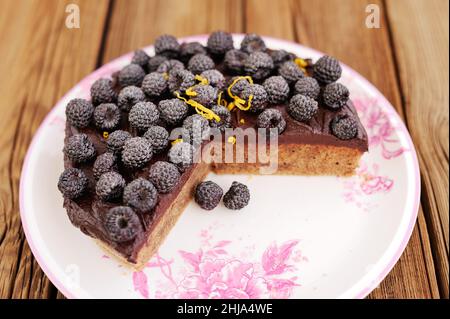 Délicieuse tarte au chocolat maison avec des mûres fraîches, du sucre glace et du zeste de citron manquant un morceau sur une table en bois horizontale Banque D'Images