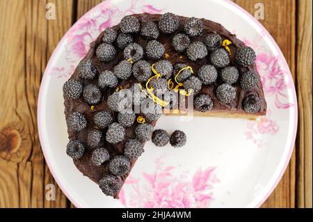 Une délicieuse tarte au chocolat avec des mûres fraîches, du sucre glace et du zeste de citron qui manque un morceau sur une table en bois Banque D'Images