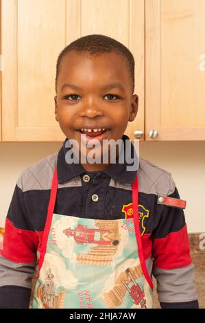 Portrait heureux d'un garçon de 4 ans en cuisine portant un tablier Banque D'Images