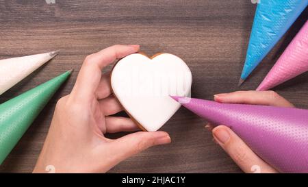 Biscuit en forme de coeur blanc à main avec cône de glaçage pour le jour de la mère, le jour de Womans ou le jour de la Saint Valentin sur fond de bois. Copier l'espace Banque D'Images