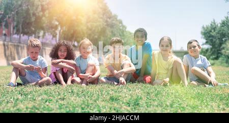 Groupe d'amis enfants heureux se reposant sur l'herbe ensemble dans le parc Banque D'Images