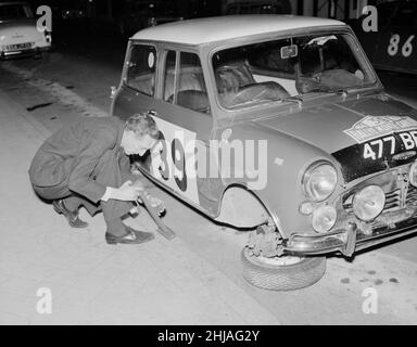 Le pilote de rallye raymond Baxter remette la roue de sa mini-voiture qui a été enlevée par d'autres pilotes alors qu'il était assis dans un bar à la fin de la course de Monte carlo.25th janvier 1964. Banque D'Images