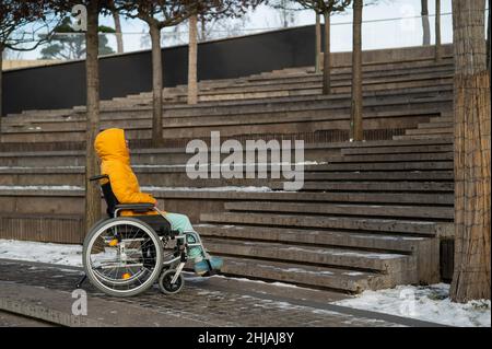 Femme en fauteuil roulant devant les escaliers dans la rue en hiver. Banque D'Images