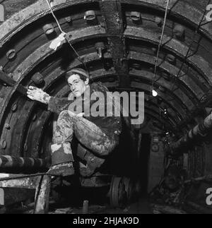 La rue n'est pas très éclairée, elle est humide et boueuse et l'humidité est élevée, mais John Upchurch 19 ans de Plumstead passe le saut dans la rue Prestage.C'est le nom de l'un des deux tunnels pilotes forés sous la Tamise pour le nouveau tunnel de Blackwall.11th mai 1962 Banque D'Images