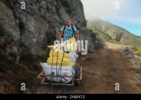 Homme avec une charrette sur le sommet du volcan actif Kawah Ijen avec une charge de soufre extrait Banque D'Images